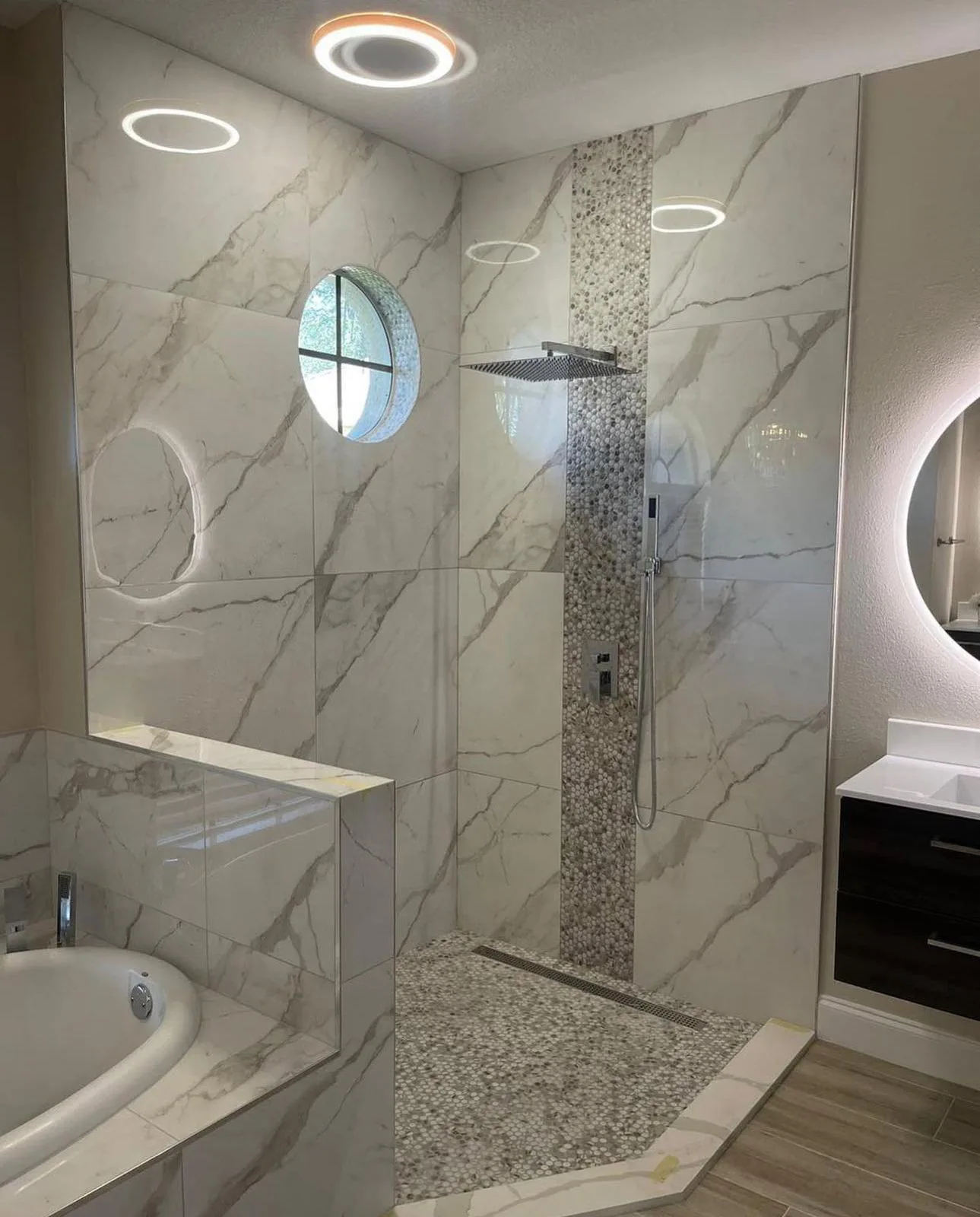 Marble-look tiled walk-in shower with rain head, pebble mosaic band and halo ceiling lights in Sarasota, FL