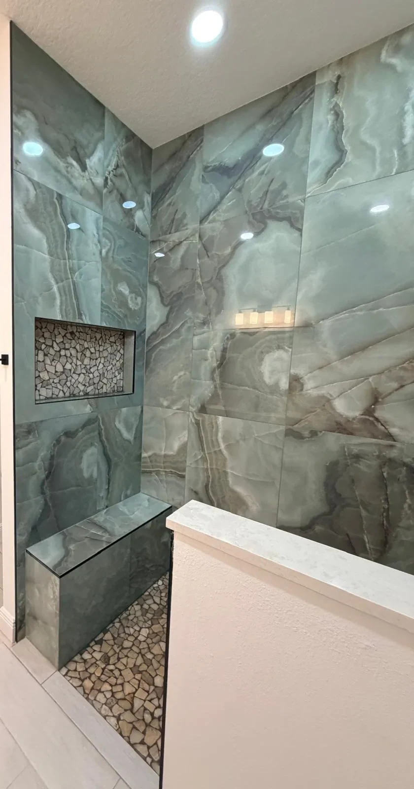 Shower wall clad in green onyx-look porcelain slabs with built-in bench and stone-chip niche in Lakewood Ranch, FL