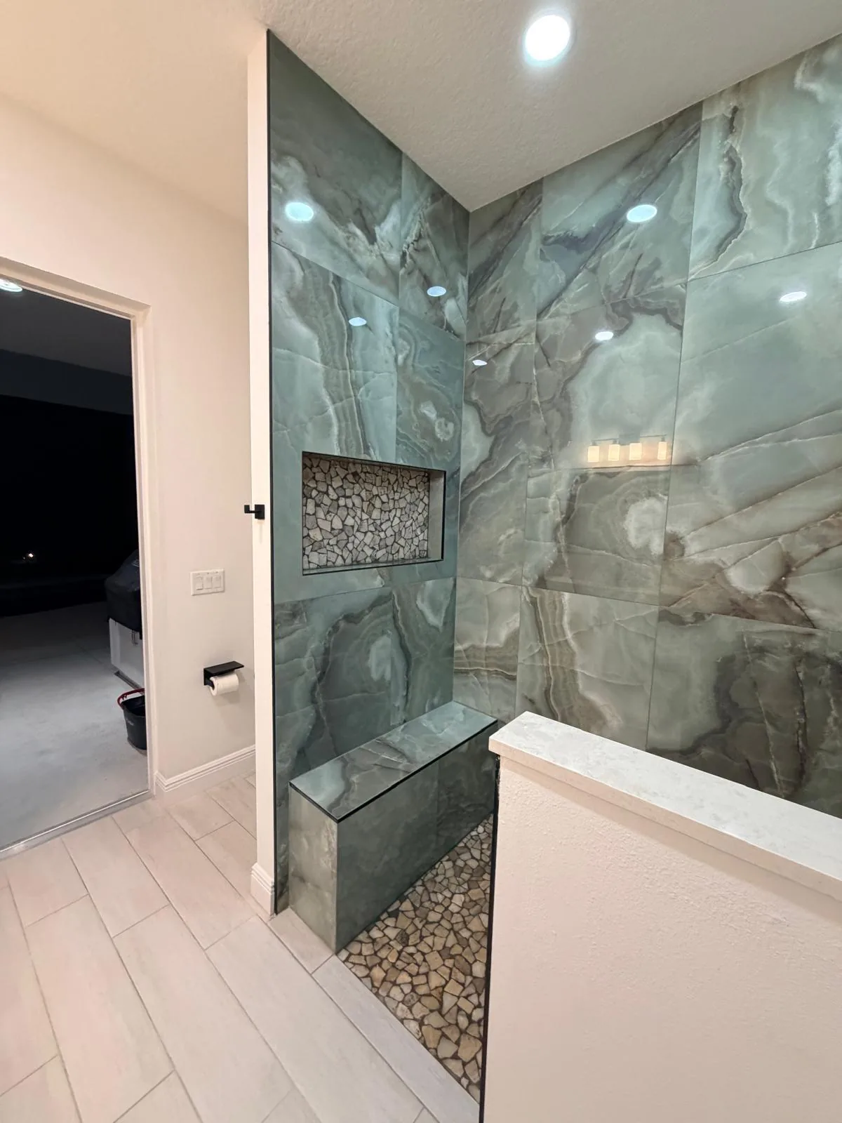 Walk-in shower clad in green onyx-look porcelain slabs with built-in bench and stone niche in Sarasota, FL