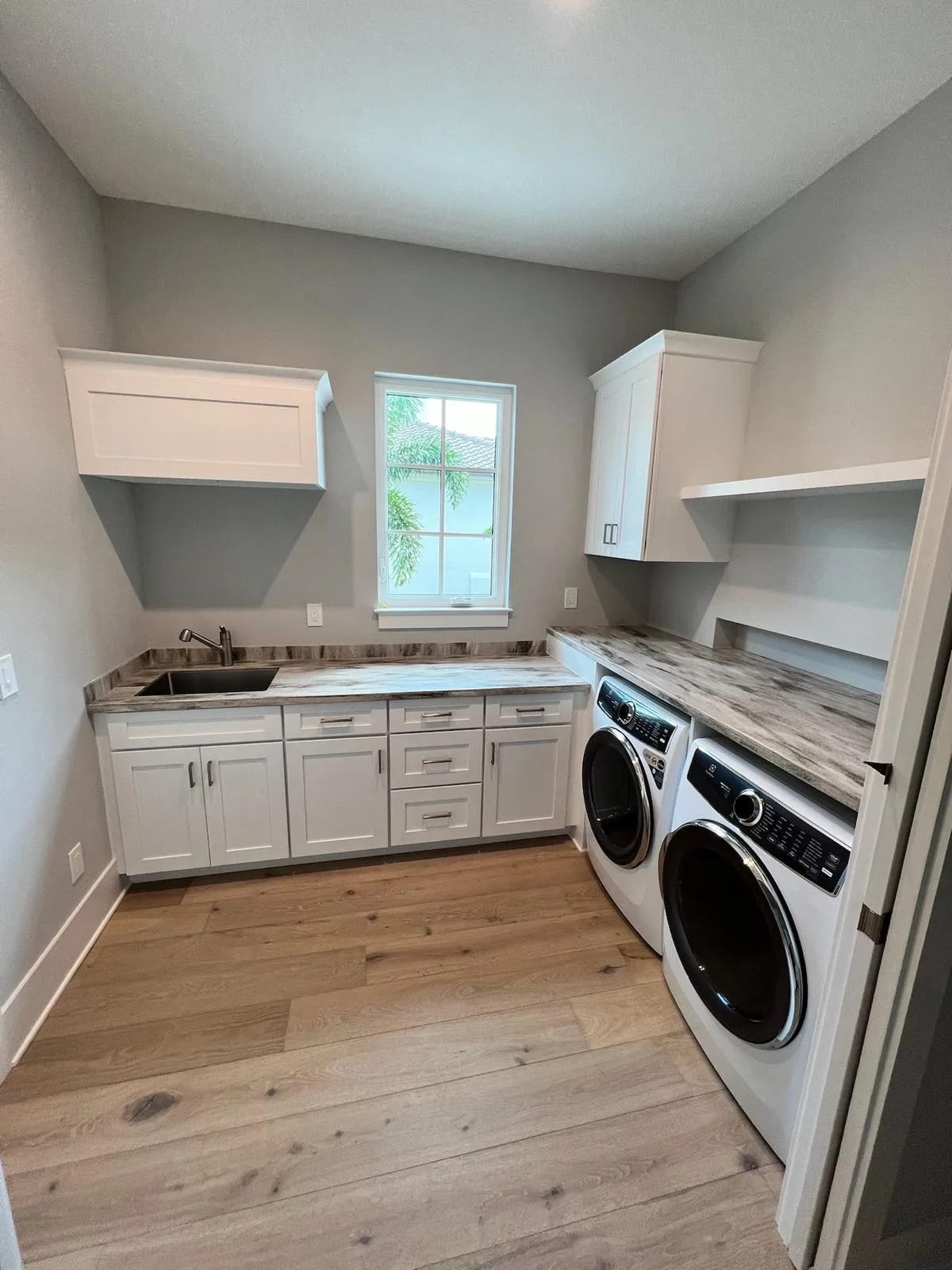 White shaker laundry room cabinets with utility sink, stone countertop, and front-load washer and dryer in Sarasota, FL