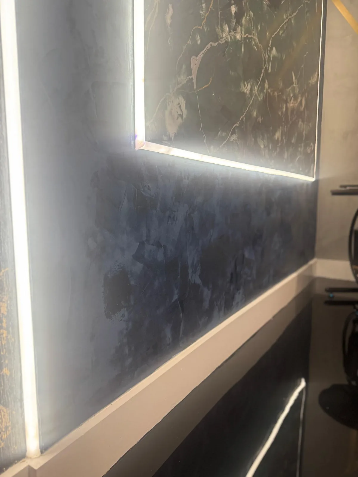 Deep navy troweled plaster wall lit by recessed LED strips below a dark marble panel in Lakewood Ranch, FL