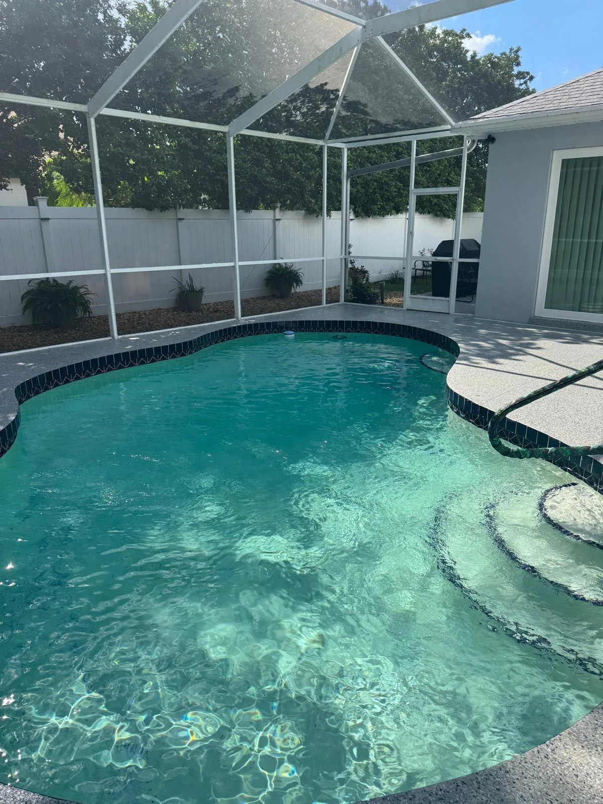 Same pool after coating, speckled gray flake deck wrapping the edge under screened enclosure in Lakewood Ranch, FL