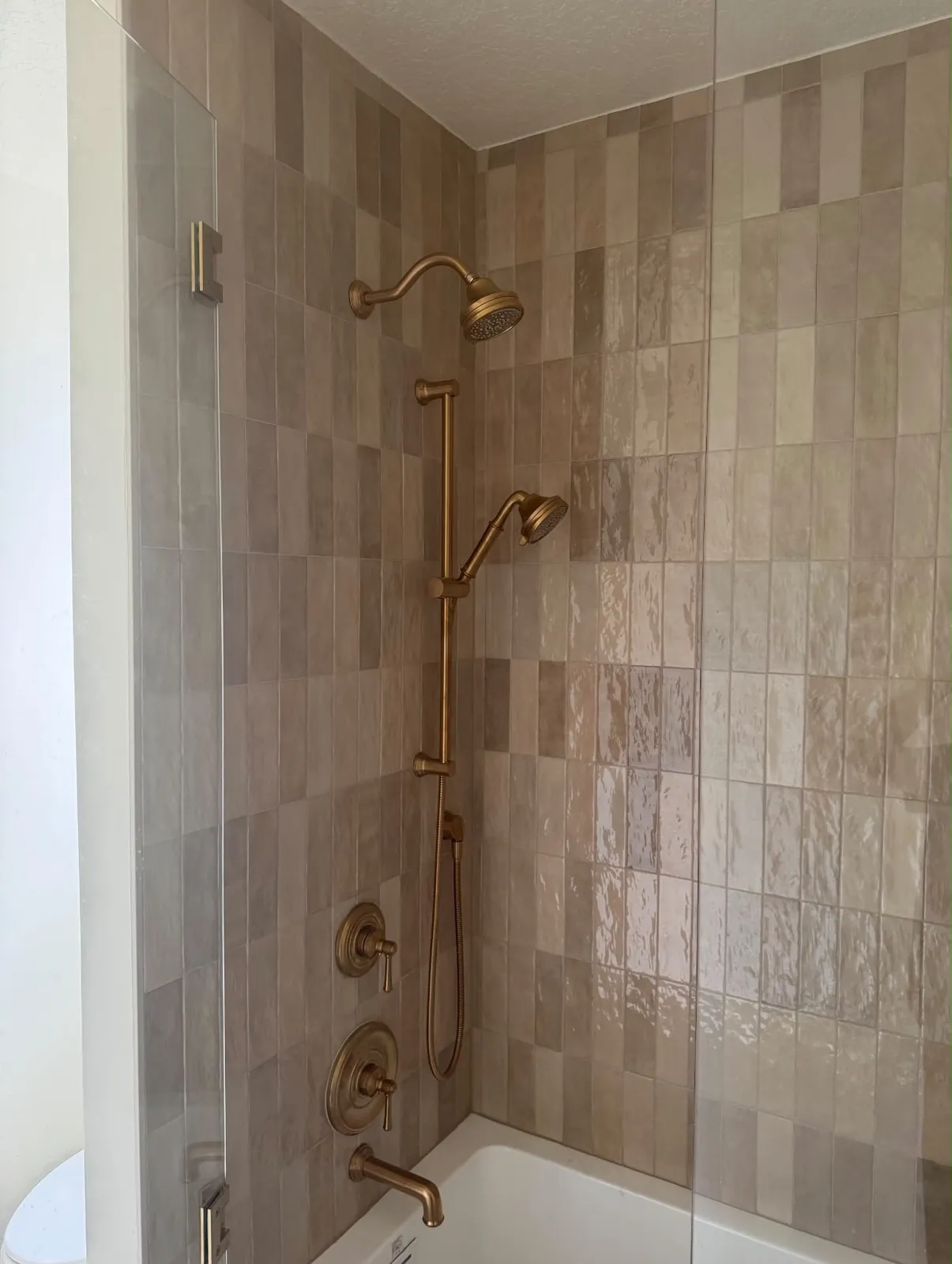 Shower tile detail with brushed brass shower fixtures and handheld sprayer
