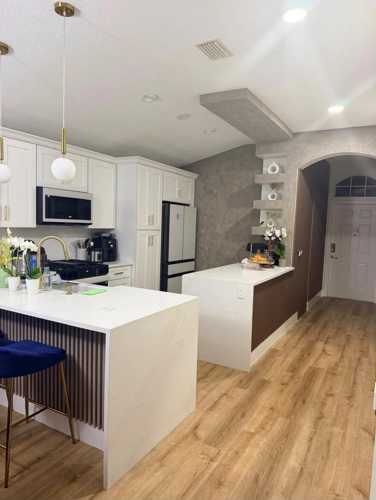 Remodeled kitchen with white quartz peninsula, reeded wood base, gold pendants and blue velvet stools in Lakewood Ranch, FL
