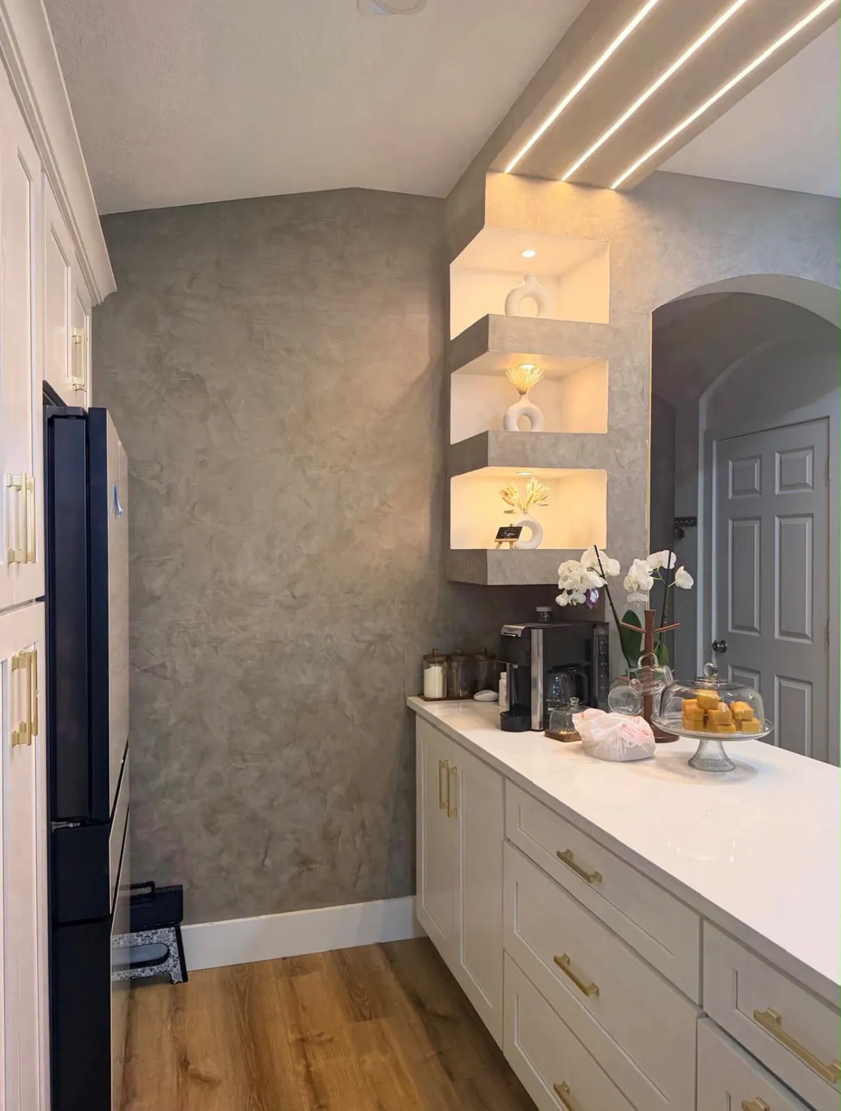 Grey polished plaster coffee bar wall with three lit niches, white cabinetry and brass hardware in Lakewood Ranch, FL