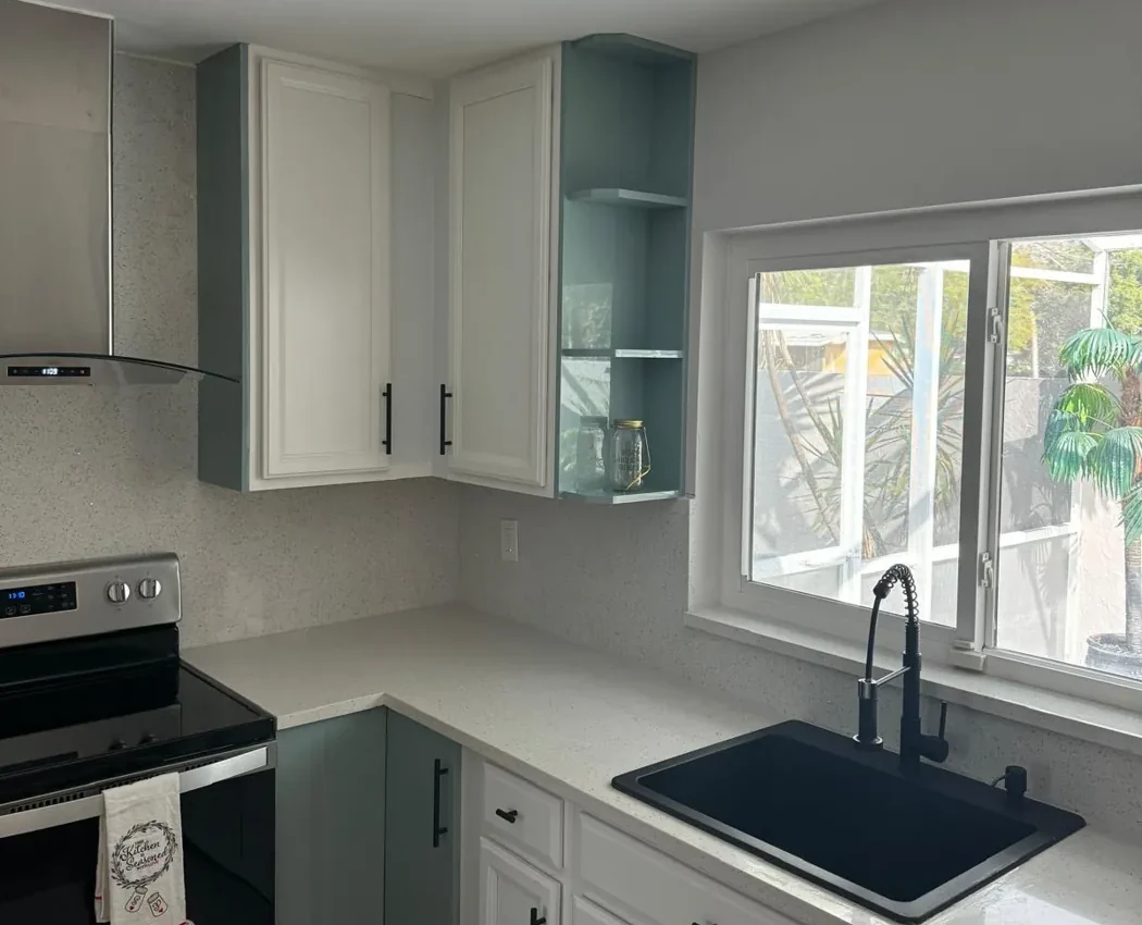 White painted upper cabinets over teal green lowers with black pulls, quartz counter and black sink in Lakewood Ranch, FL