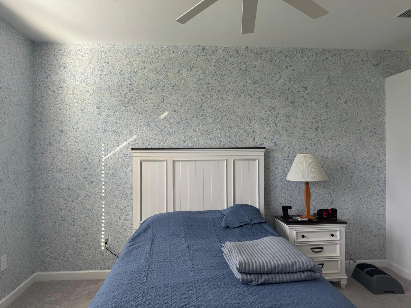 Bedroom walls finished in light blue speckled liquid wallpaper with white headboard and nightstand in Lakewood Ranch, FL