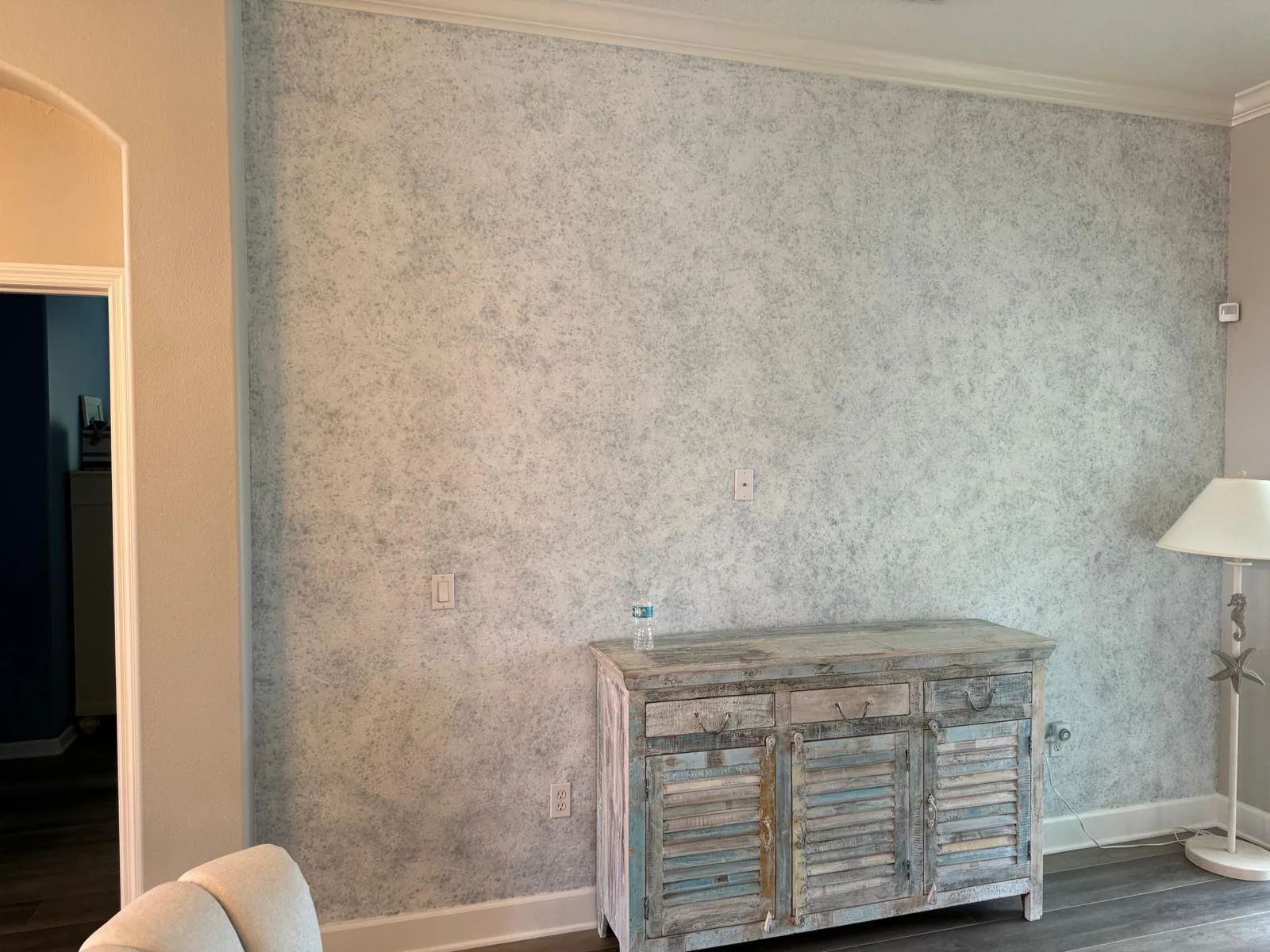 Living room feature wall in soft warm gray mottled texture beside a distressed coastal sideboard in Lakewood Ranch, FL