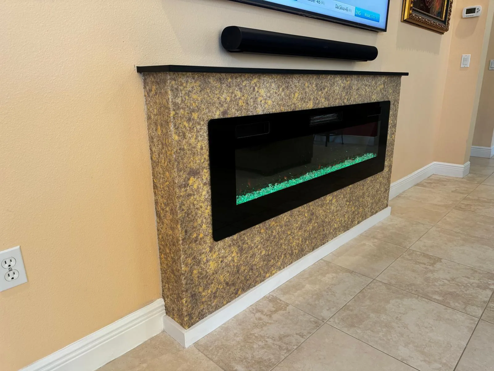 Electric fireplace surround wrapped in beige and gold flecked wall texture with black stone top in Lakewood Ranch, FL