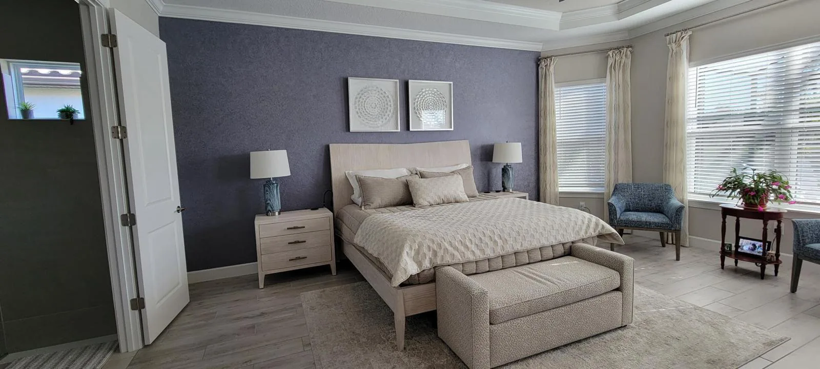 Bright master bedroom with a soft gray-violet textured accent wall behind a light wood bed in Lakewood Ranch, FL