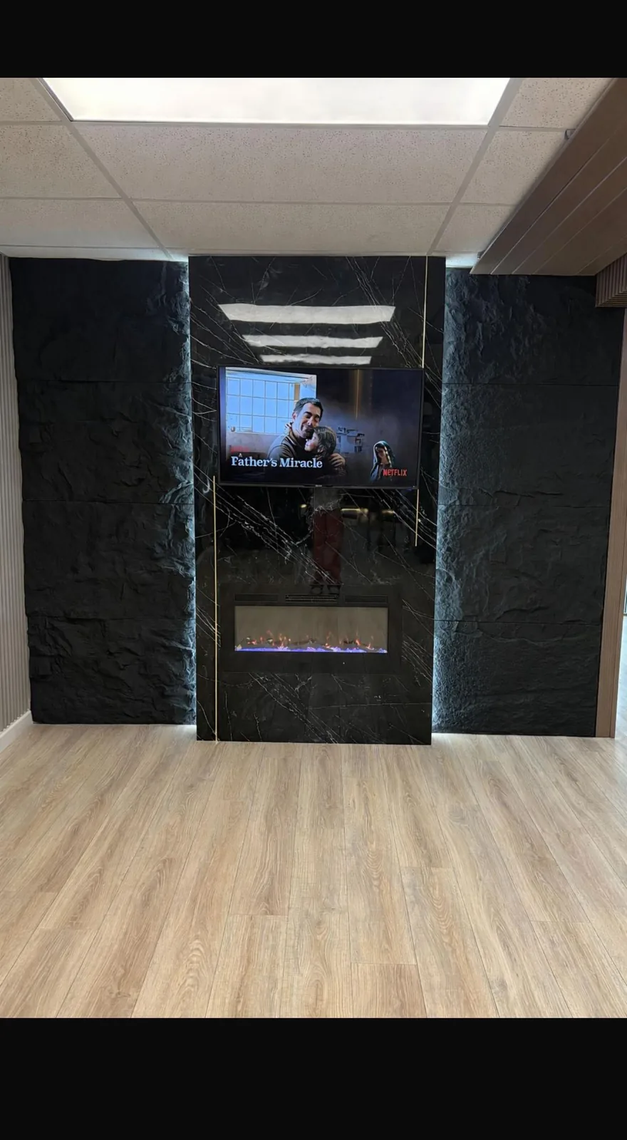 Black marble-look panel wall with TV, linear fireplace, gold inlays and backlit black stone panels in Lakewood Ranch, FL