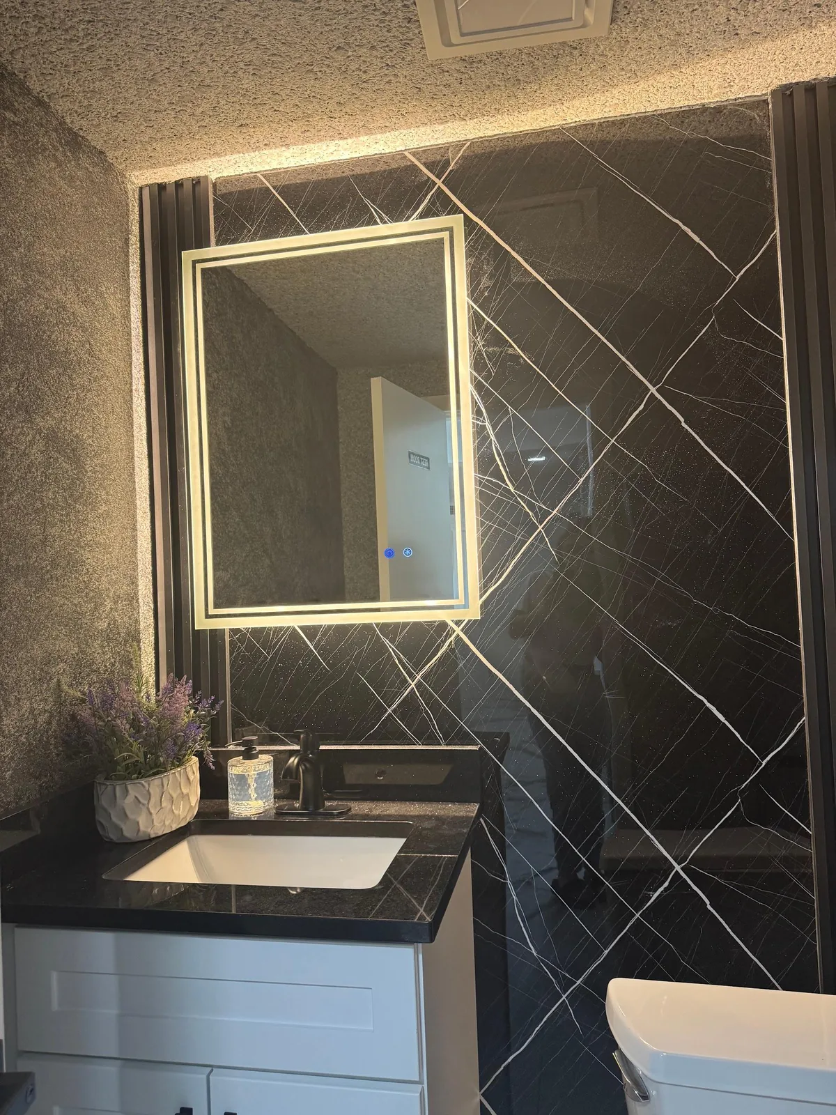 Powder room with black marble-look panel wall, fluted reveals, backlit LED mirror and white vanity in Lakewood Ranch, FL