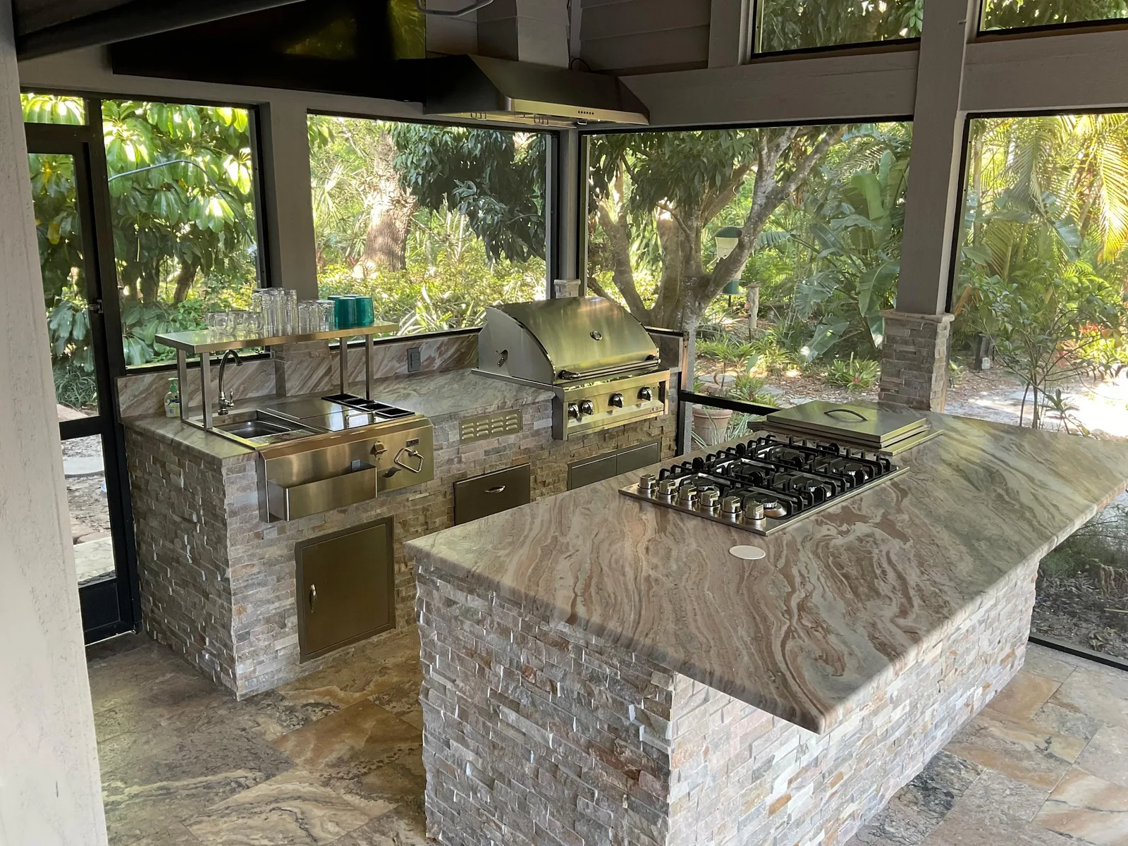 Covered outdoor kitchen with stacked stone base, natural stone countertops, stainless grill, cooktop and vent hood in Sarasota, FL