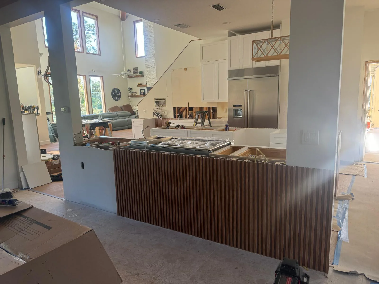 Open-concept kitchen mid-renovation with fluted wood island base, white cabinets, floor protection and tools in Lakewood Ranch, FL