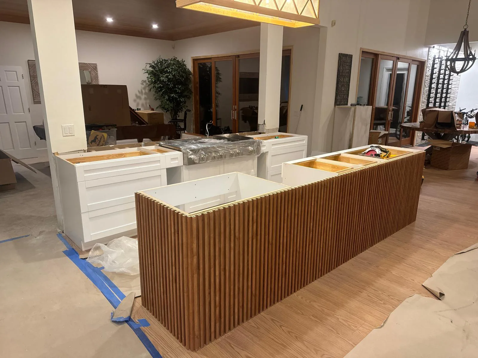 Kitchen island wrapped in vertical wood slat panels beside open white cabinet boxes during installation in Lakewood Ranch, FL