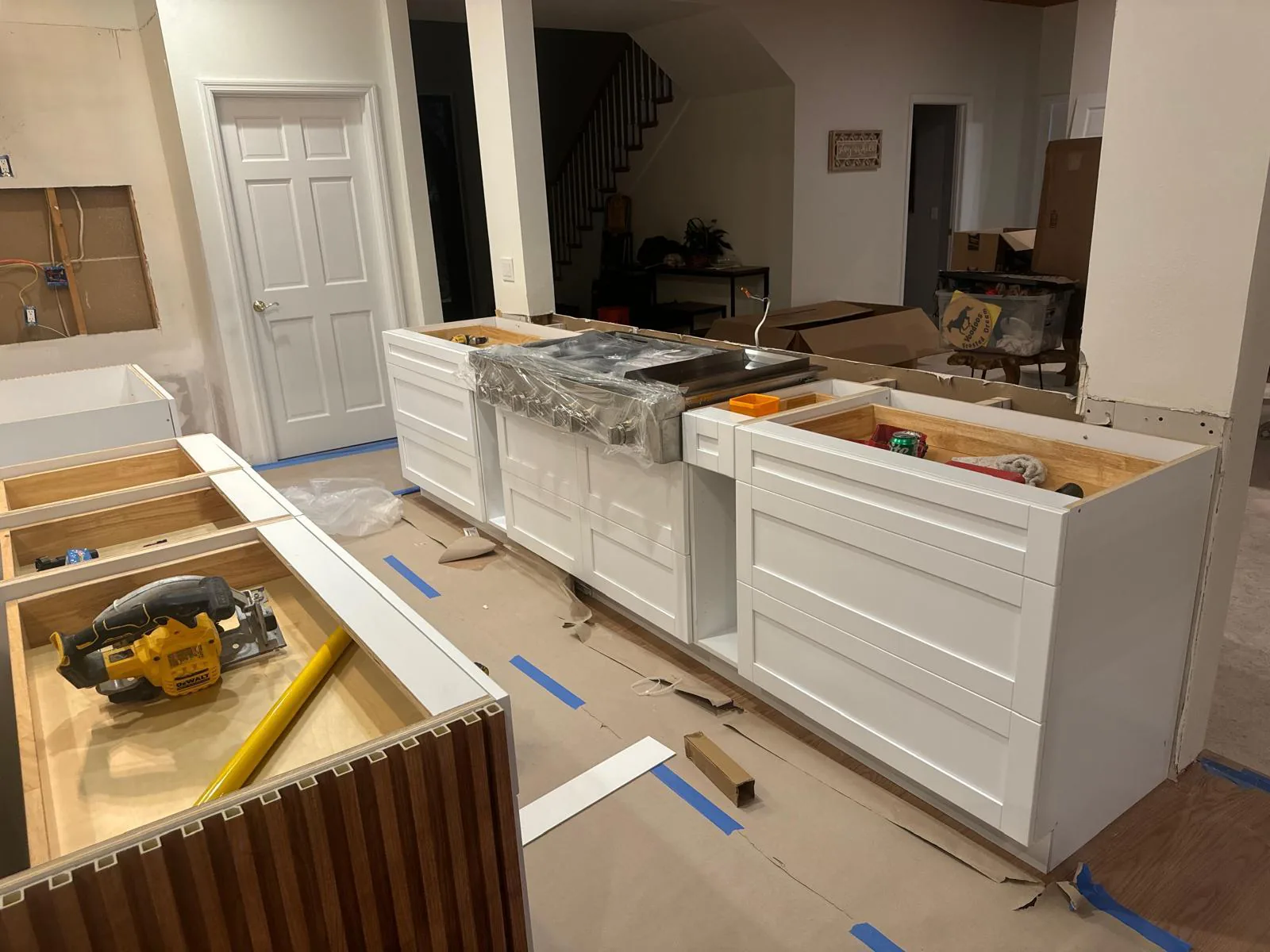 White painted base cabinets set in a row on paper-protected floors with a cordless saw nearby in Lakewood Ranch, FL