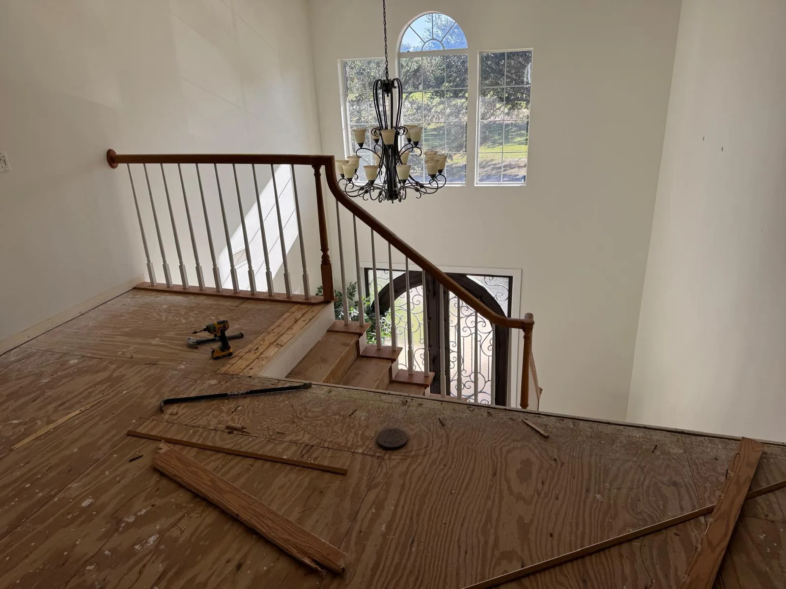 Two-story foyer during demolition with exposed plywood subfloor, old wood railing and hanging chandelier in Lakewood Ranch, FL