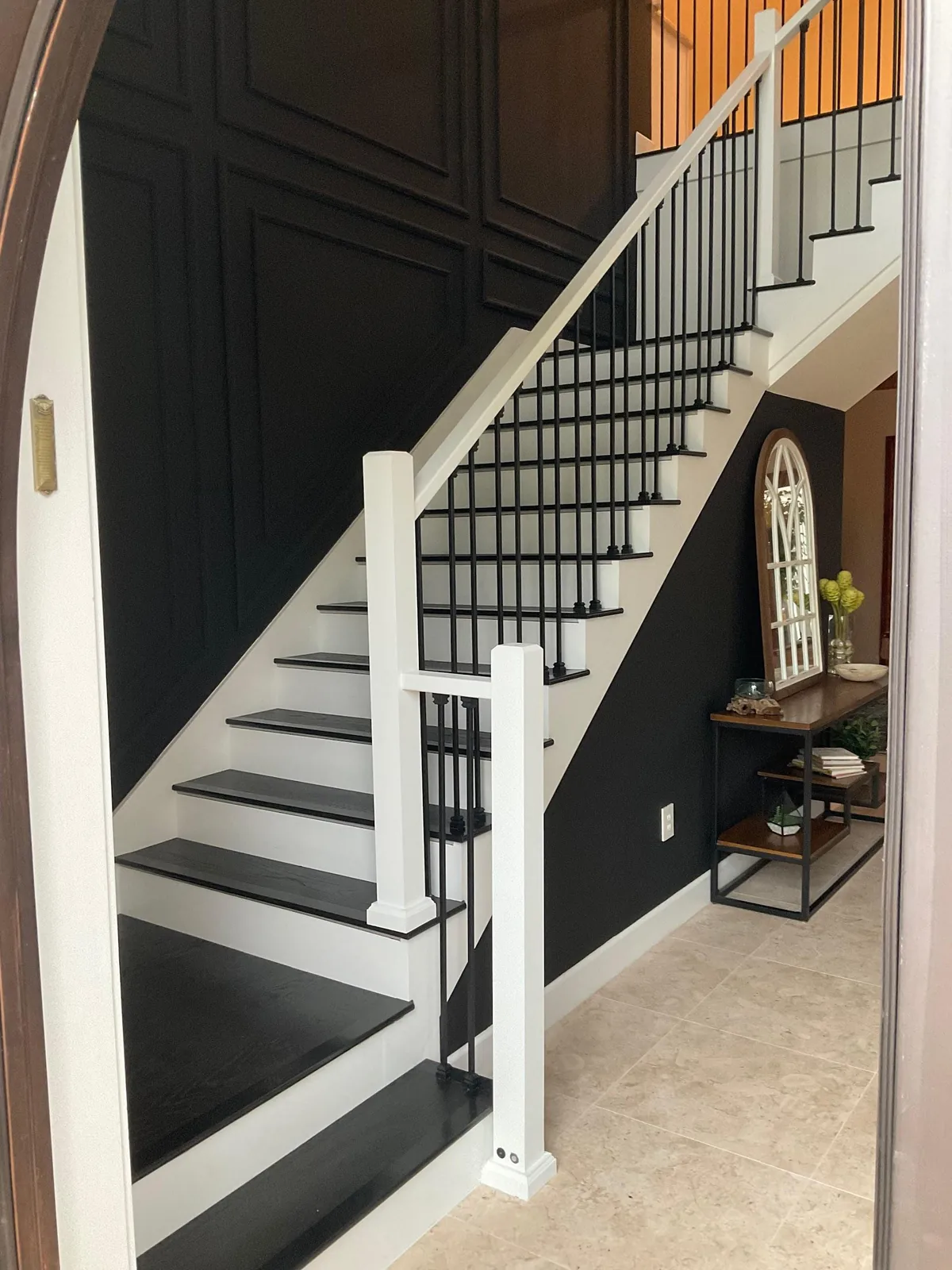 Remodeled foyer staircase with black treads, white risers, iron balusters and dark paneled accent wall in Lakewood Ranch, FL