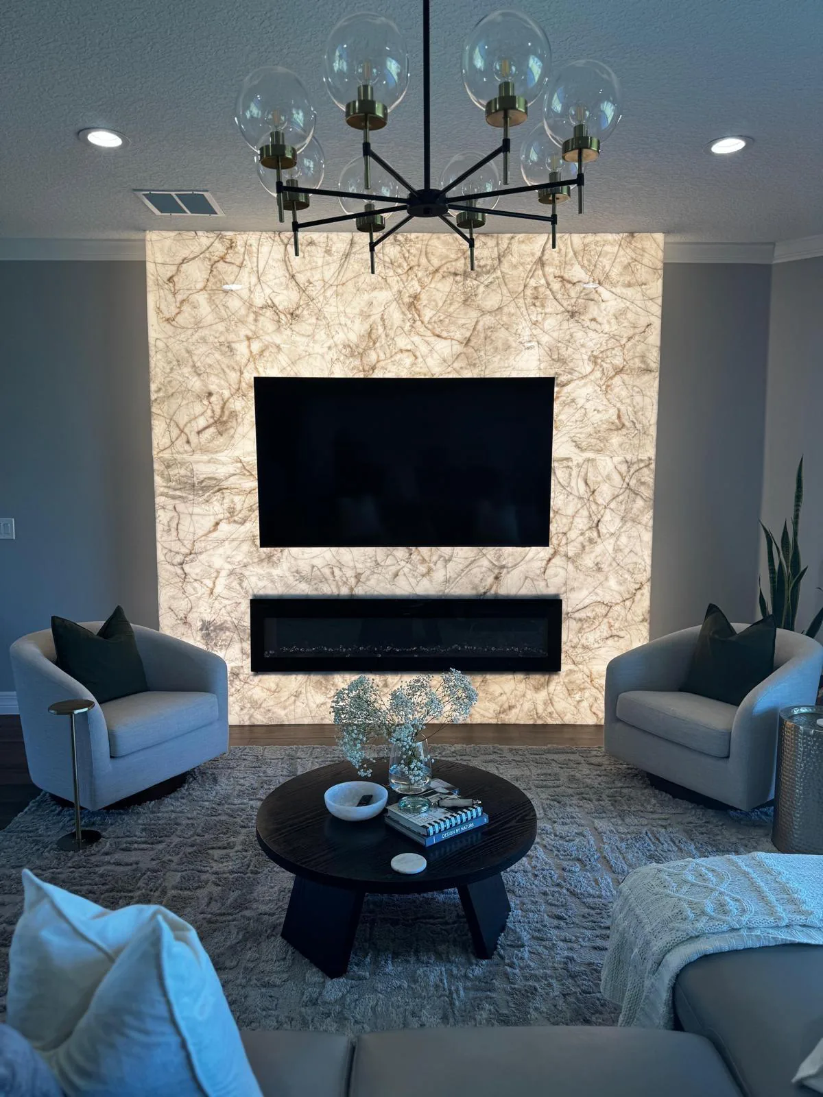 Backlit translucent stone panel wall glowing behind a mounted TV and black linear fireplace in Sarasota, FL
