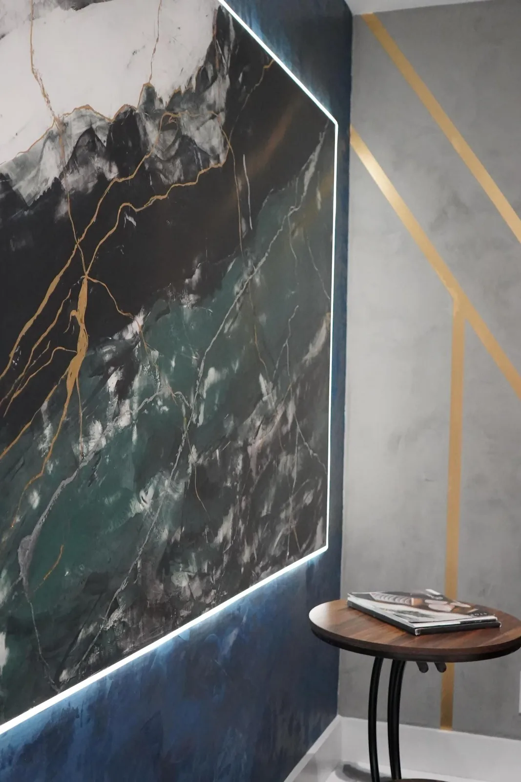 Backlit marble-effect art panel in black and green over navy plaster beside brass-striped grey wall in Sarasota, FL