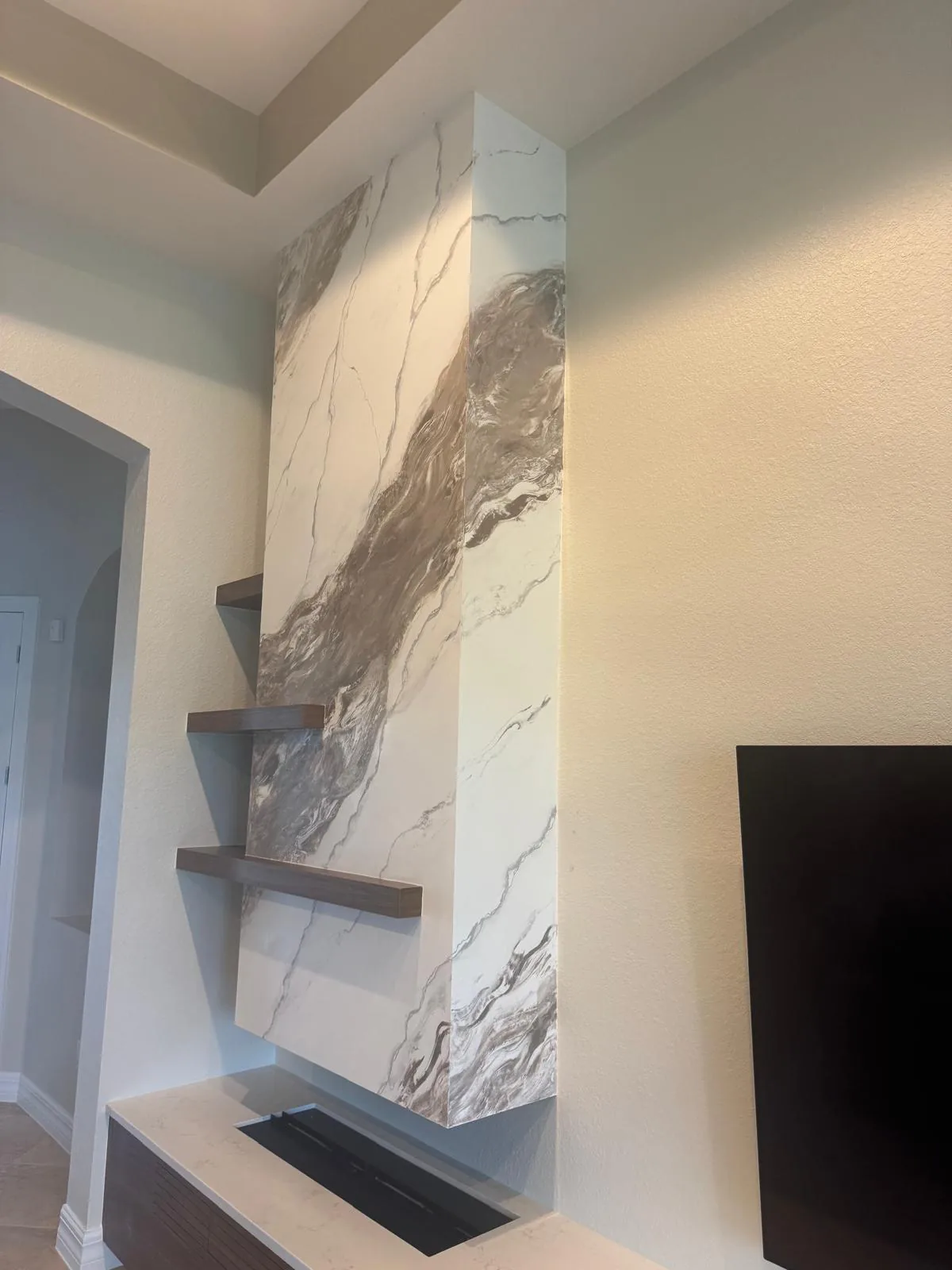 White and brown marble-effect fireplace column wrapping the corner with three floating walnut shelves in Lakewood Ranch, FL