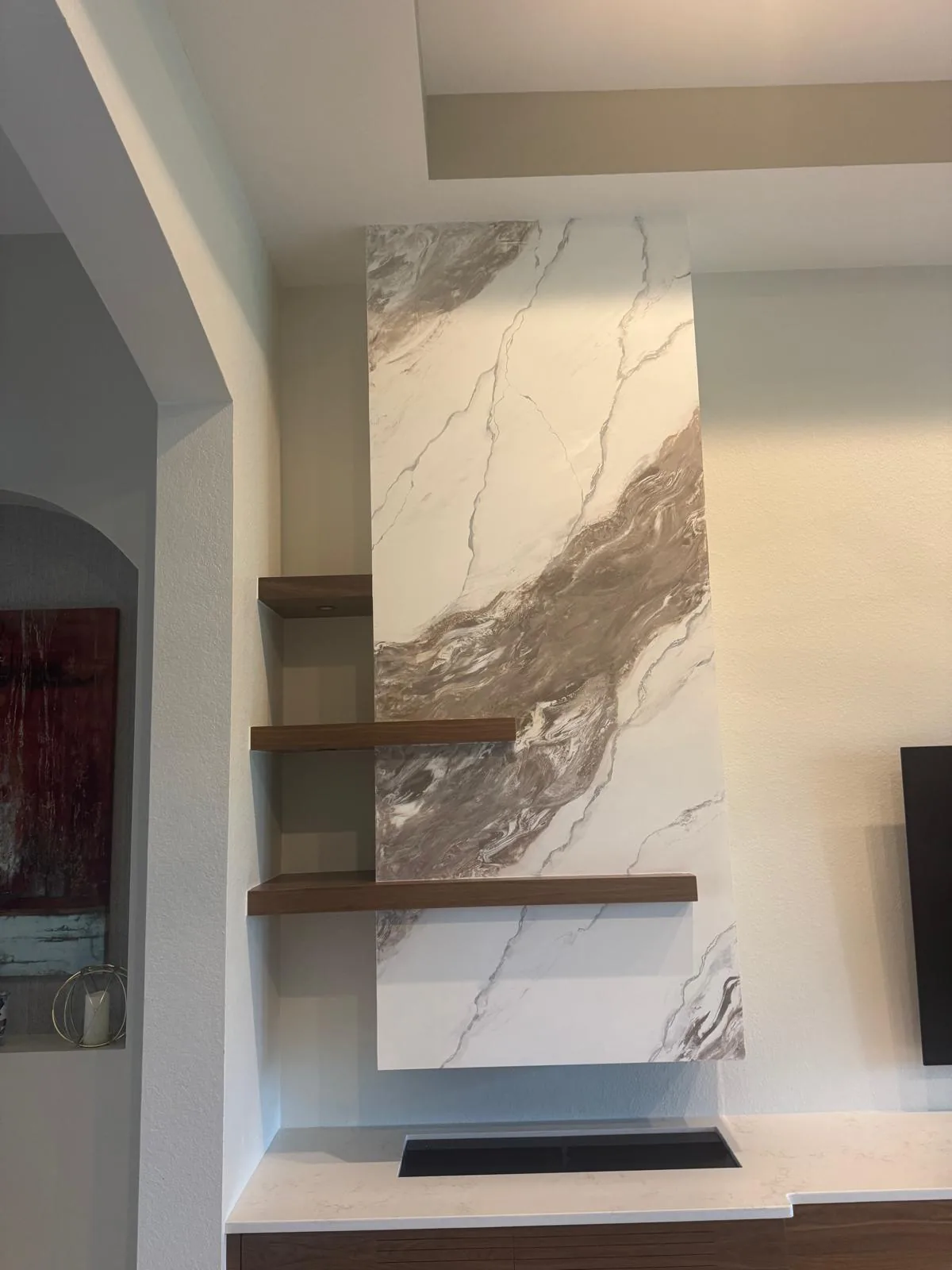 Tall marble-look plaster fireplace column with three floating walnut shelves and linear electric fireplace in Lakewood Ranch, FL