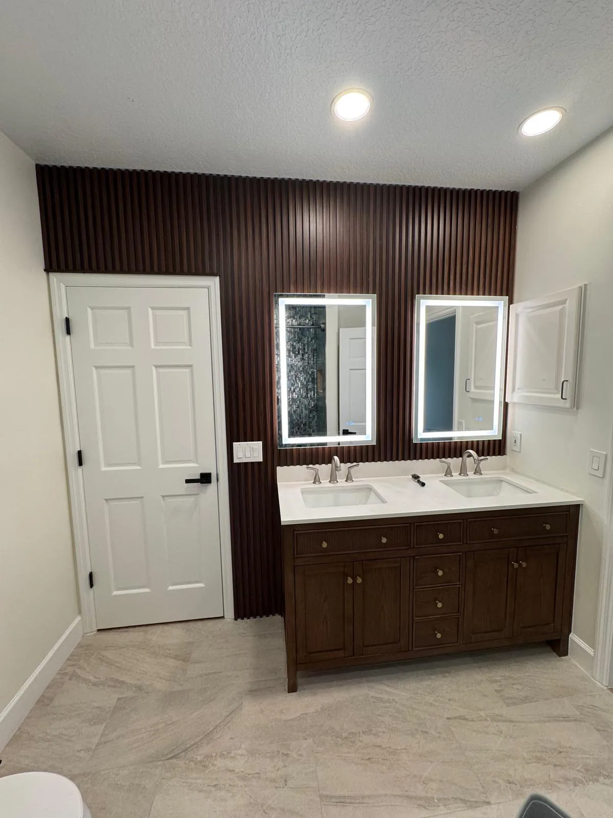 Bathroom with dark brown fluted slat accent wall, two backlit LED mirrors and wood double vanity in Lakewood Ranch, FL